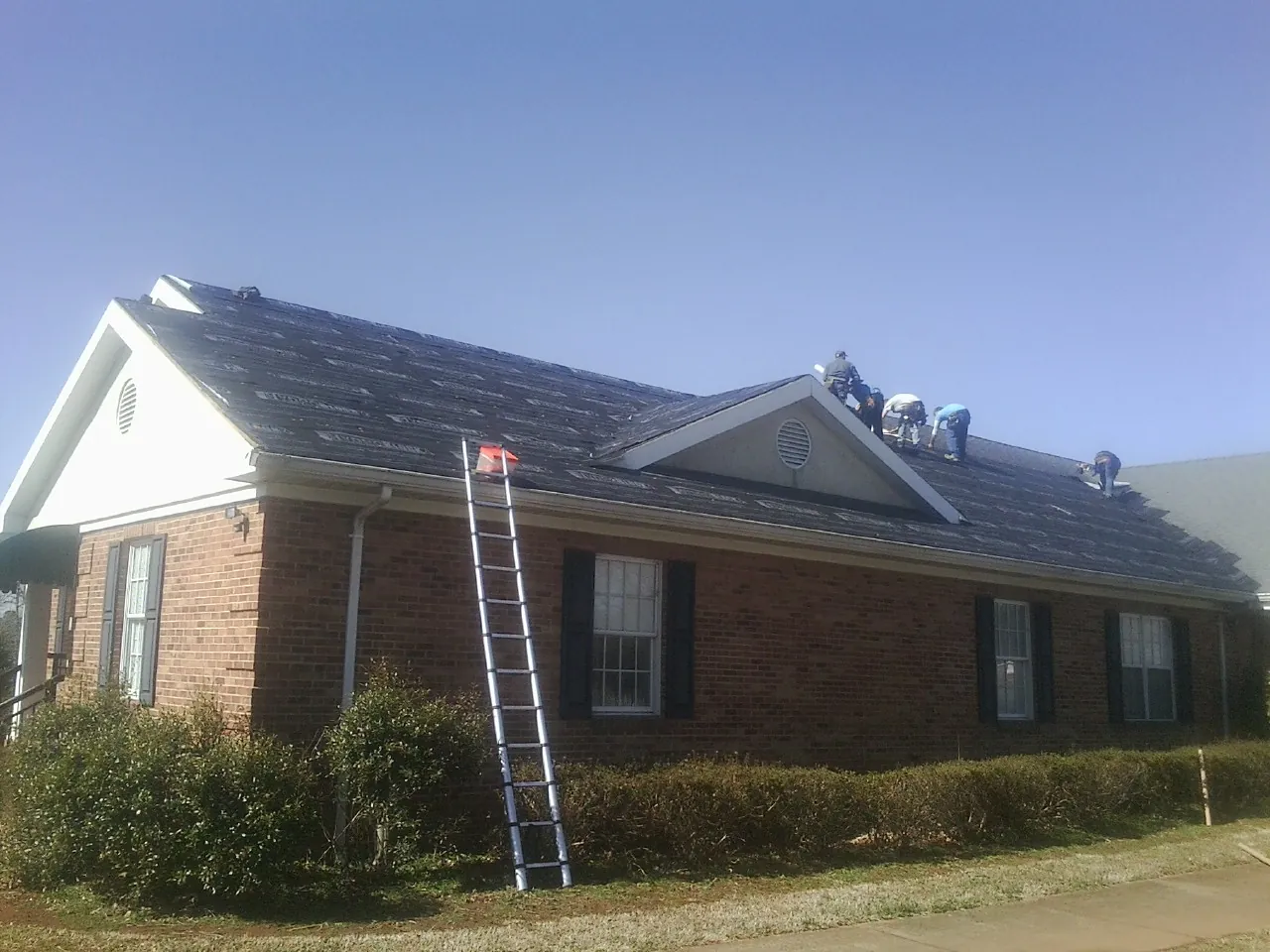 Crew tearing shingles off a brick ranch roof with a ladder set — Metal Roof Repair work by our crew in Delmar