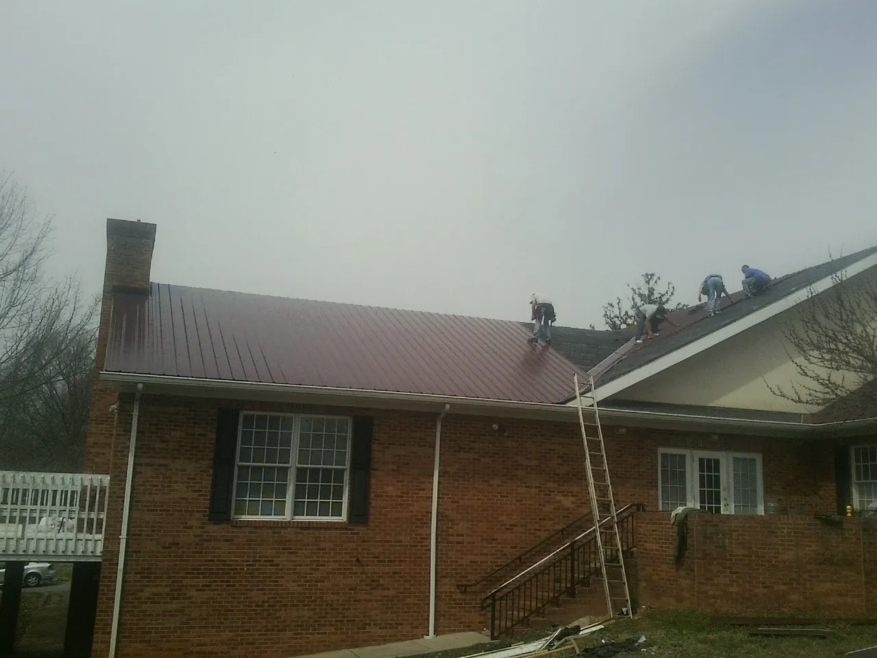 Crew setting red metal roofing panels on a brick home in Delmar